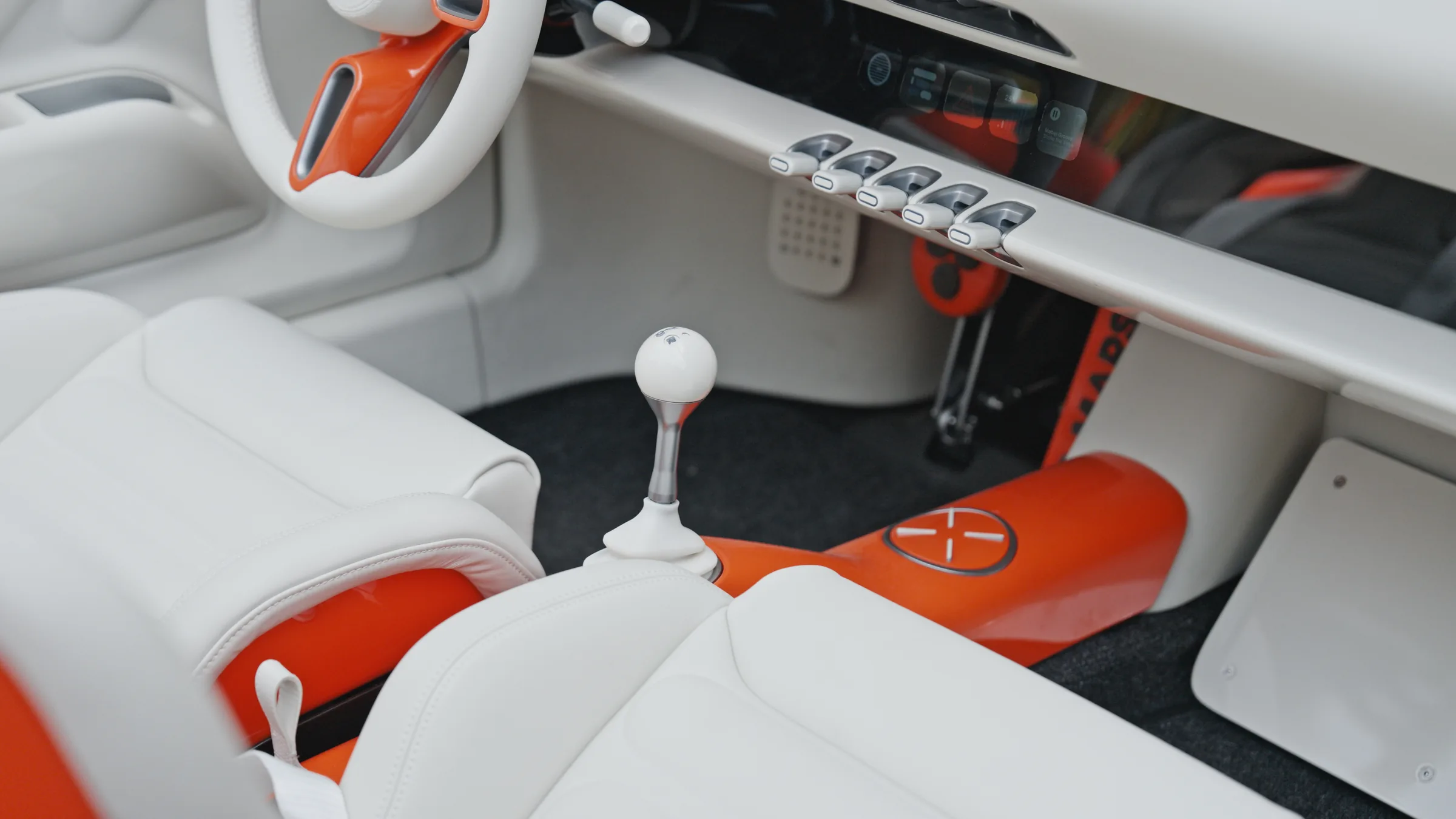 Cream Napa interior with a vermilion-lacquered tunnel, piano-key switches under the dash and a white ball-topped selector