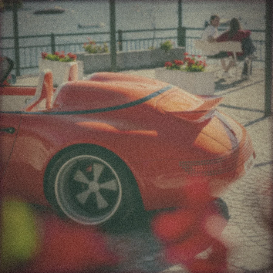 Polaroid: the Funkster's tail on a lakeside terrace, geraniums in front and a couple on a bench behind